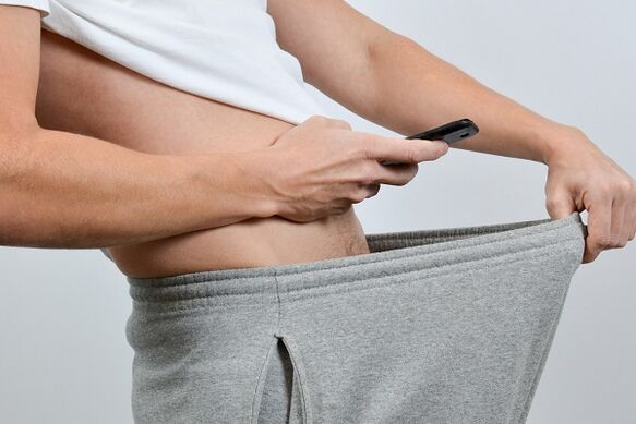 um homem olha para baixo das calças e vê um pênis aumentado